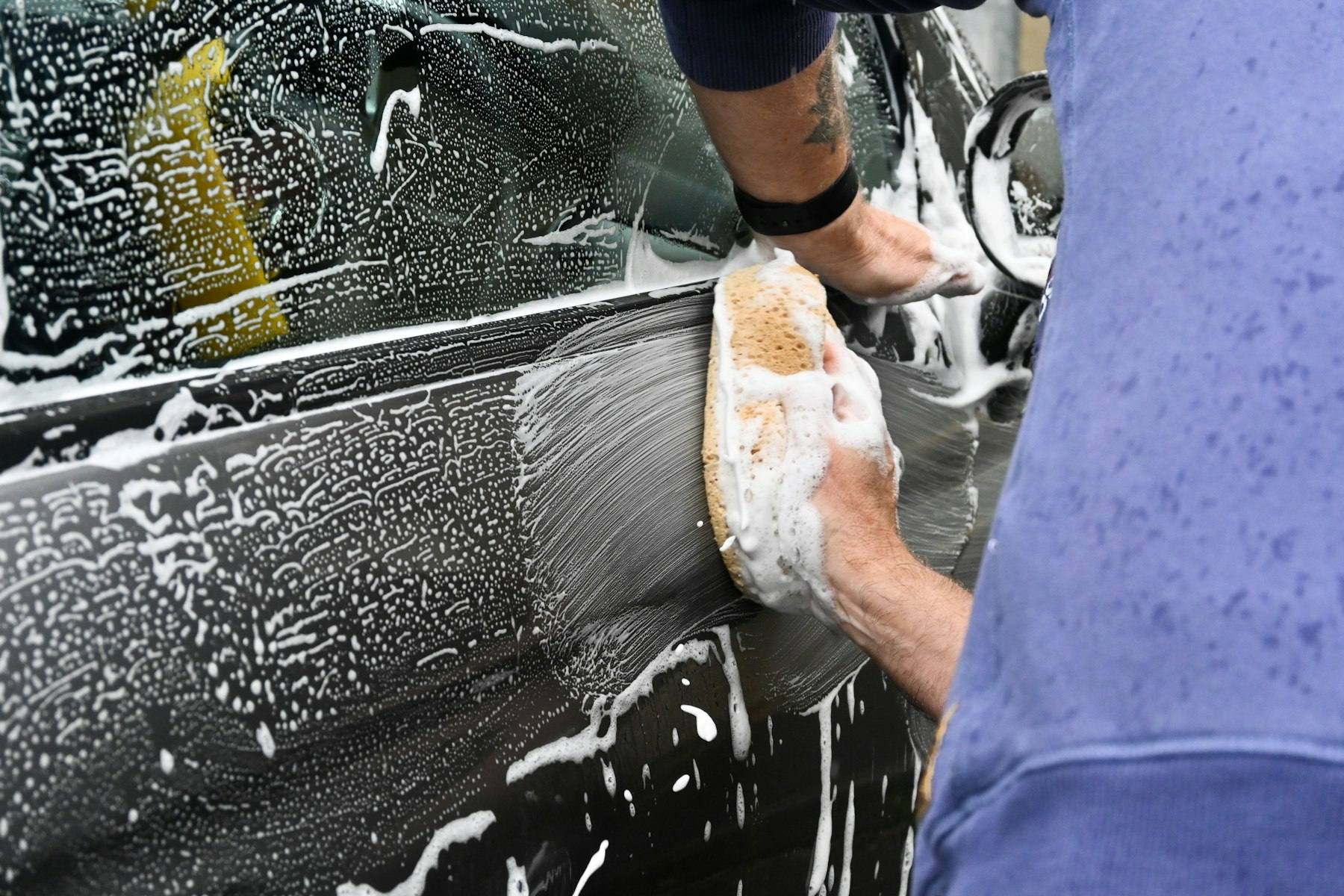 Detailer hand-washing a car with a foam mitt