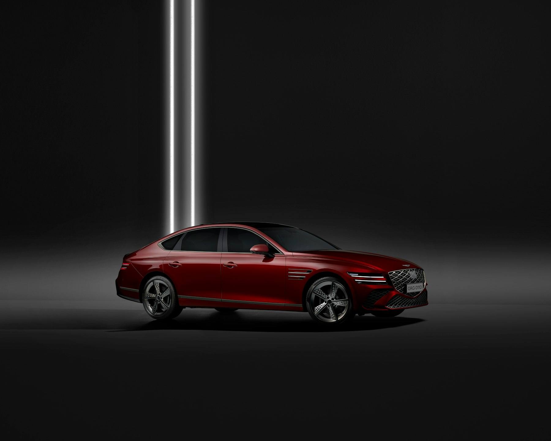 Red sedan lit by a single vertical light in a dark studio